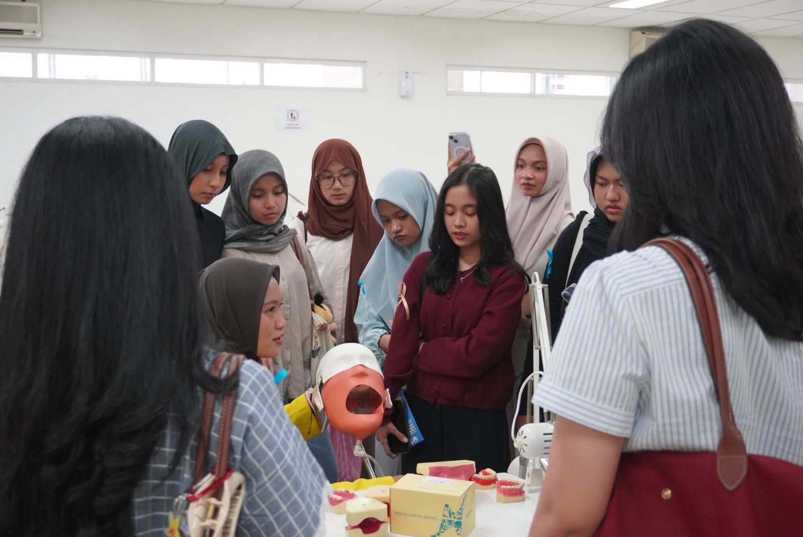 Peserta mengerumuni meja berisi phantom head dan model gigi saat demonstrasi alat